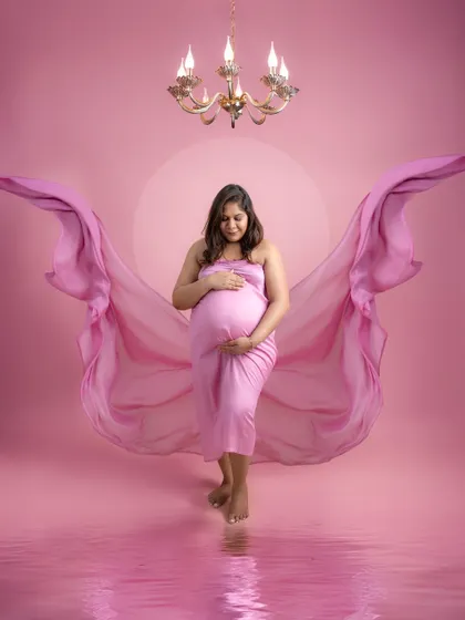 A dreamy and ethereal portrait. The mother-to-be stands in a pool of soft pink light, with fabric wings flowing behind her, creating an angelic and serene image.