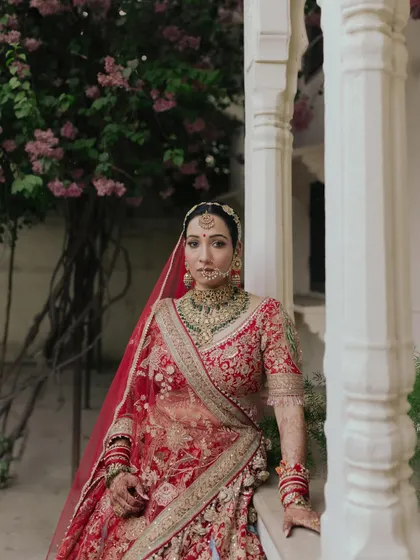 A portrait of Rakhi in her ornate red lehenga, set against the classic architecture of Jaipur. The image feels both timeless and deeply rooted in heritage.