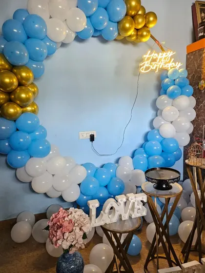 A simple and sweet birthday setup with a blue, white, and gold balloon ring. The 'LOVE' sign and cake stands make it a perfect corner for cake cutting at a home party.