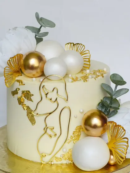 A gorgeous and elegant baby shower cake in white and gold. The design features a modern line-art topper of a mother-to-be, surrounded by delicate flowers.