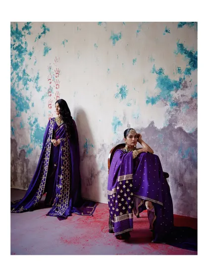 Two models showcase the versatility of our purple sarees. One is a classic drape, while the other features a heavily embroidered shawl, demonstrating different ways to style these heritage pieces.