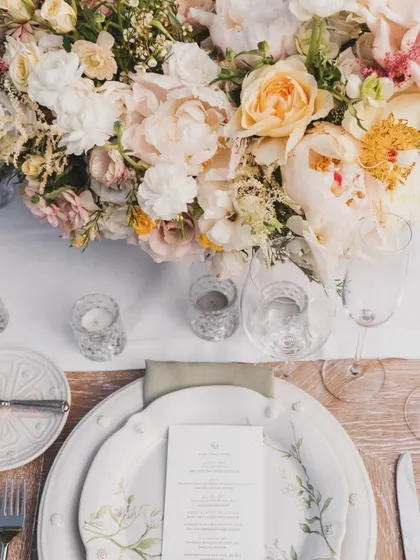 An overhead view of a place setting, highlighting the beautiful pastel floral centerpiece and the intricate details on the charger plates.