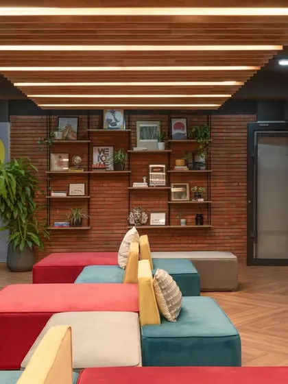 This huddle area combines comfortable, modular seating with an exposed brick wall and a stylish bookshelf, creating a relaxed setting for informal team collaboration.