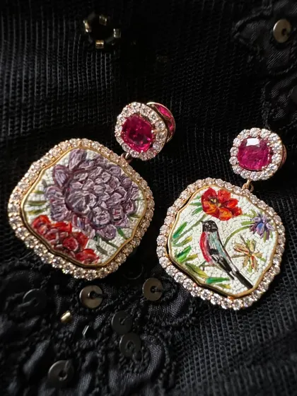 This pair of micromosaic earrings features a bird and a chrysanthemum, set against a dark background. The design is framed by natural diamonds and topped with Mozambique rubies, creating a dramatic effect.
