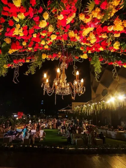 A breathtaking view of a rooftop reception at Jade Gardens. The floral archway, illuminated by a grand chandelier, frames the entire celebration, with the open sky and city lights providing a stunning natural backdrop.