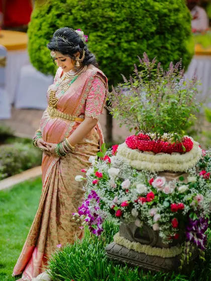 A traditional maternity shoot look, with the expecting mother standing by a Tulasi plant. She looks serene and beautiful.