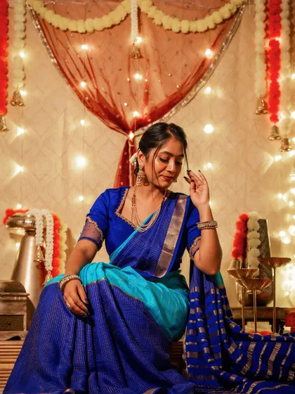 A moment of quiet reflection during Deepavali. The light from the diyas catches the beautiful texture of the blue silk saree, creating a warm and serene festive mood.