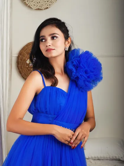 A close-up portrait of a model in the royal blue one-shoulder gown, showing the handcrafted floral detail.