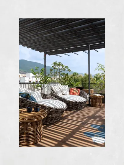 The terrace lounge at Kamala Residence was designed as a serene retreat from the city. A metal pergola frames the view of the Tirupati hills and mitigates sunlight, while cane furniture enhances the tropical theme.