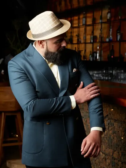 A clean cut and a confident fit. This image captures a client wearing the deep teal suit in a relaxed, stylish setting, defining modern sophistication.