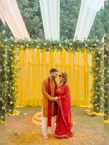 A lovely portrait of the couple standing together against a backdrop of marigold decorations at their haldi ceremony. Their coordinated outfits and happy smiles make for a perfect picture.