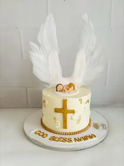 A serene and beautiful baptism cake with a golden cross, delicate angel wings, and a sleeping baby topper.