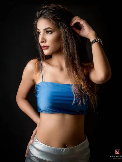 A classic studio portrait against a black background, highlighting the contrast of the blue satin top. The model's pose is confident and timeless, showcasing a fierce yet graceful look.