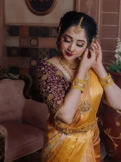 A close-up of a beautiful bride in a yellow silk saree and a contrasting purple embroidered blouse. The zardosi work on the blouse is completely customized.