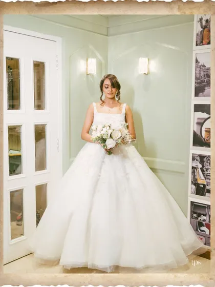 A classic, full-length bridal portrait. The bride's elegant gown and serene expression are beautifully captured, with a vintage-style border adding a touch of nostalgia.