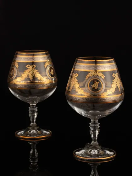 A pair of exquisite brandy glasses with gold detailing, shot against a pure black background. This technique, known as low-key photography, creates a feeling of luxury and sophistication.