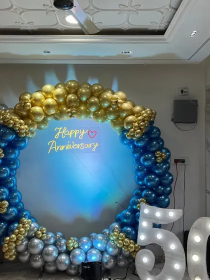 I also cater to anniversaries, like this elegant 50th anniversary celebration. The setup features a full balloon ring in gold and blue, a 'Happy Anniversary' neon sign, and large marquee numbers to mark the golden milestone.