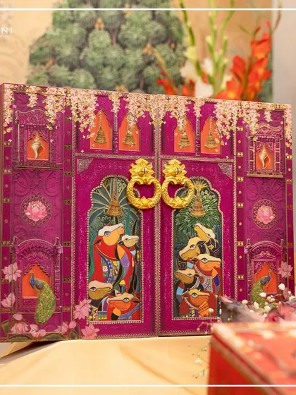 An exquisite wedding invitation hamper from my Pichwai collection. The ornate doors, adorned with traditional art and featuring golden handles, open to reveal a world of celebration, setting a tone of opulence and cultural richness.