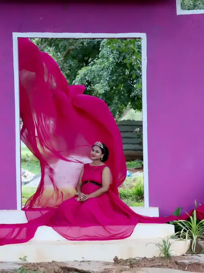 A creative maternity shot using a purple wall with a window cutout, with the pink fabric of the gown flowing through.