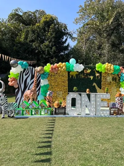 The main stage for a "Wild One" jungle birthday, featuring large animal props, a foliage wall, and "ONE" in marquee letters.