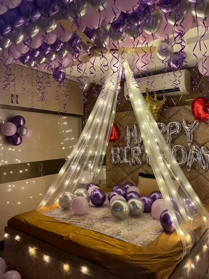 A purple and silver themed birthday room, featuring a fairy light canopy over the bed and dozens of balloons on the ceiling.