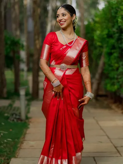 A stunning bride in a vibrant red silk saree, walking through a garden path. We love capturing these candid-style portraits that feel full of life and movement.