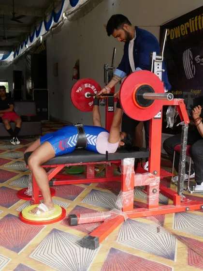 A spotter assists me during a heavy bench press at a district-level competition. Safety and support are crucial.