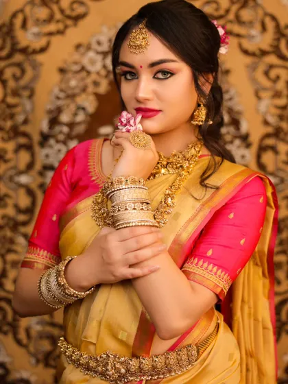 An elegant portrait of a model in a golden silk saree. Her pose, holding a flower, and the intricate temple jewelry create a look of classic grace and beauty.