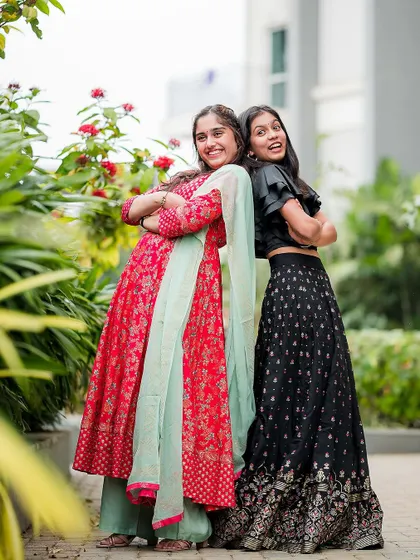 A full-length shot of two sisters posing back-to-back, showcasing their vibrant traditional outfits and infectious laughter.