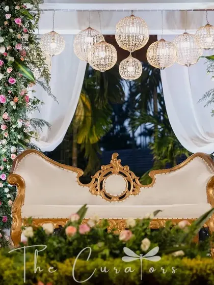 A close-up of our elegant reception stage, featuring a classic gold and white sofa, flanked by towers of white and pink roses and modern slatted screens.
