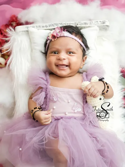 A beautiful baby girl in a lavender tutu, smiling in her sleep. Lying on a bed of soft clouds and surrounded by flowers, this is a truly dreamy and ethereal newborn portrait.