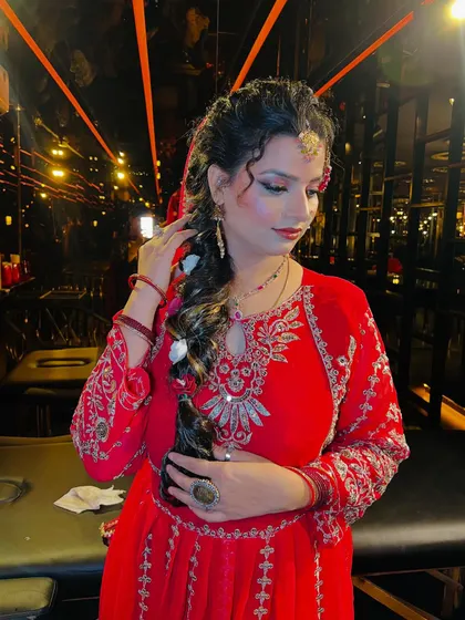 A candid moment showing the bride adjusting her hair, adorned with white flowers. This highlights the beautiful contrast between the red outfit and the soft floral accessories in her braid.