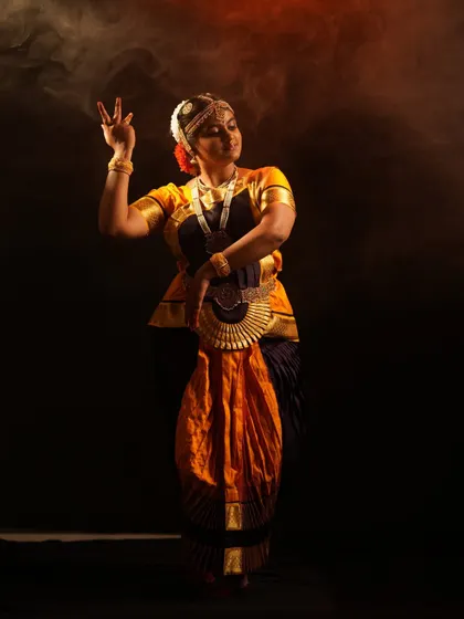 A full-length view of the Bharatanatyam costume, showcasing the traditional draping and jewelry in a dynamic dance posture against a smoky, atmospheric background.
