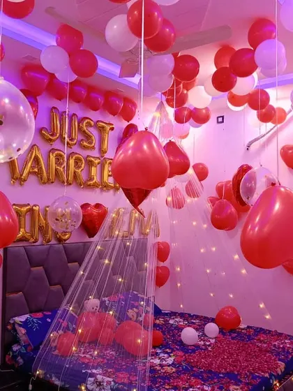 A "Just Married" bedroom decoration. The room is filled with red and white balloons, a light-up canopy, and personalized foil letters on the bed.