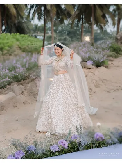 A bride playing with her veil against a backdrop of palm trees and lavender flowers. A whimsical and romantic portrait.
