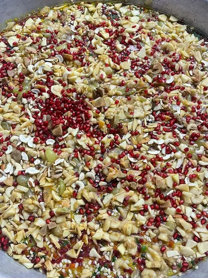 A large bowl of our special fruit and nut salad. It's a refreshing and healthy dessert option, generously topped with pomegranate seeds and chopped nuts.