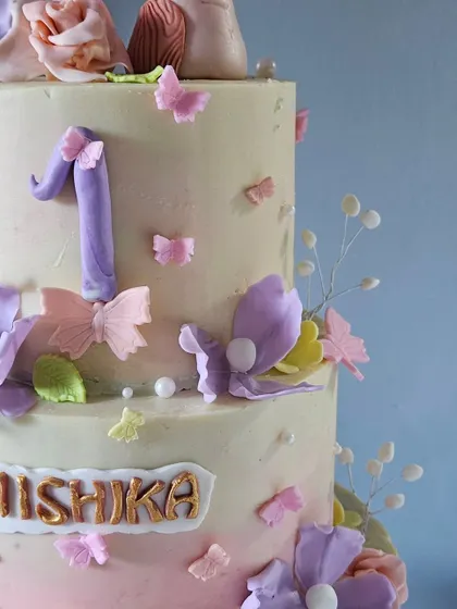 This close-up shows the personalized name plaque and the number "1" on the enchanted garden cake, surrounded by tiny butterflies and flowers.