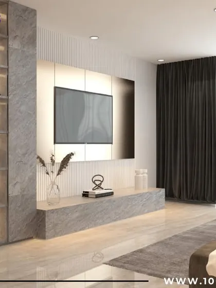 A living room from our 'Zen Glam' project, showcasing a minimalist TV unit set against a textured grey wall. The tall, illuminated display cabinet adds verticality and a touch of glamour.