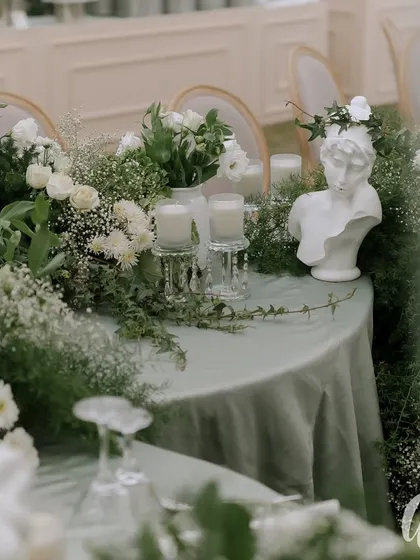 A small detail showing a classical bust adorned with a crown of fresh flowers, placed on a table. This is an example of how we weave thematic elements throughout the decor.