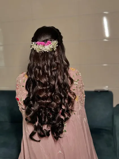 A view of her hairstyle from the back, featuring soft curls and a beautiful arrangement of fresh baby's breath and pink flowers.