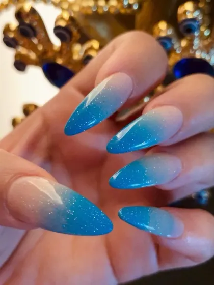 Blue glitter ombré on sharp stiletto nails. The gradient effect from a natural base to a sparkling blue tip is both striking and elegant.
