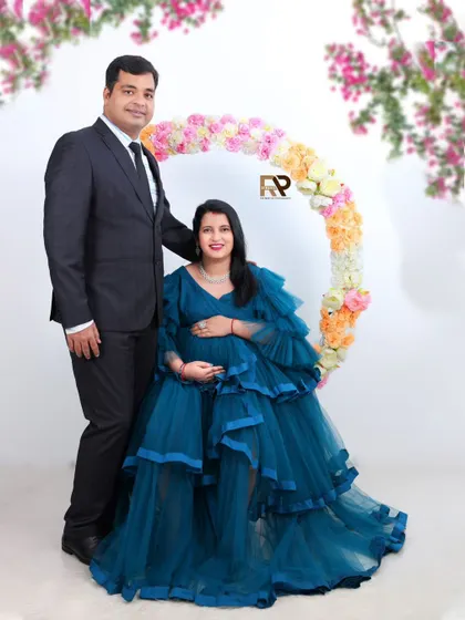 A beautiful family portrait. The couple stands together in front of our floral hoop prop, with the mom-to-be looking stunning in her blue ruffled gown.