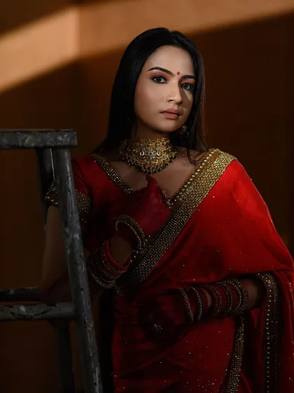 A full-length shot from our conceptual red saree series. The dramatic lighting and the rustic ladder prop add an industrial-chic vibe to the traditional attire.