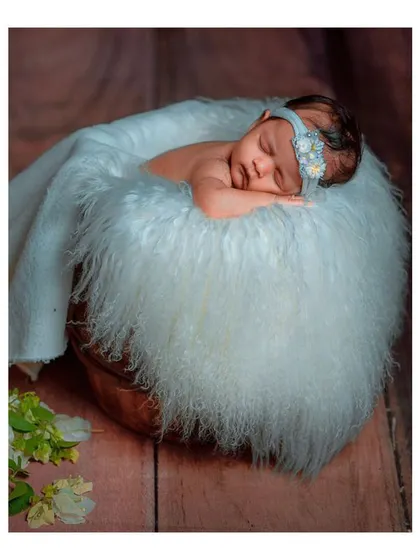 A newborn sleeping peacefully in a rustic bucket lined with soft white fur.