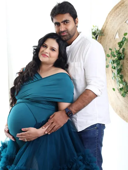 A close-up portrait focusing on the couple's connection and the baby bump. The teal wrap-style gown beautifully complements the bright, natural-light studio setting.
