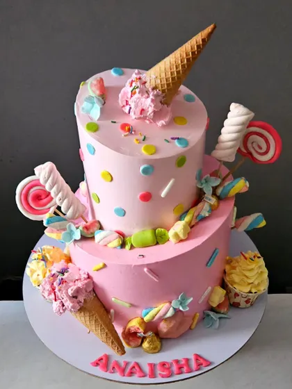 A full view of the two-tier topsy-turvy candyland cake, made with pink whipped cream and decorated with edible sweets.