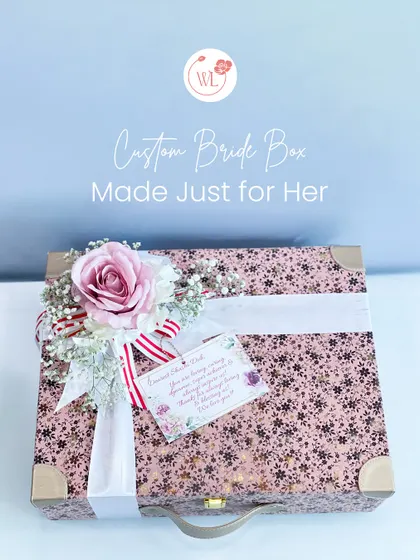 A custom bride box, made just for her. This beautiful floral-printed trunk is adorned with a large rose and a personalized tag, promising a treasure trove of goodies inside.