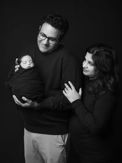 A classic family pose with the father holding the baby while the mother looks on with love. This black and white composition is elegant and timeless.
