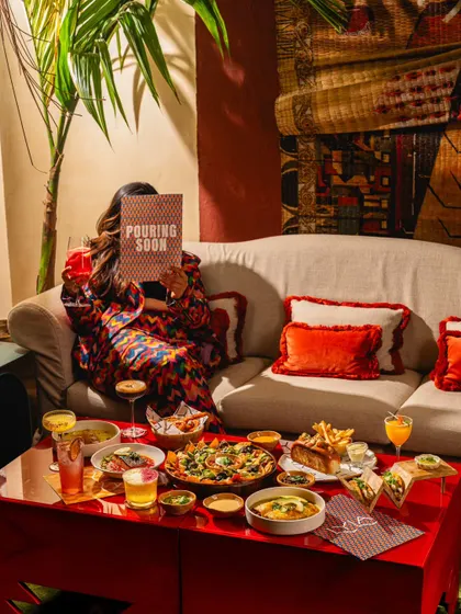 A vibrant, maximalist scene at Lyla Bombay, showing a full spread of food and drinks. This image captures a fun, celebratory mood, perfect for group outings.