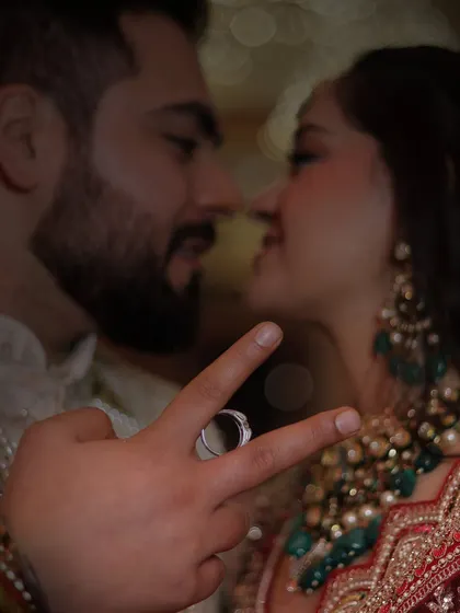 A creative and intimate couple portrait. The focus is on the engagement ring held between the groom's fingers, with the couple sharing a close moment in the background. A very artistic shot.